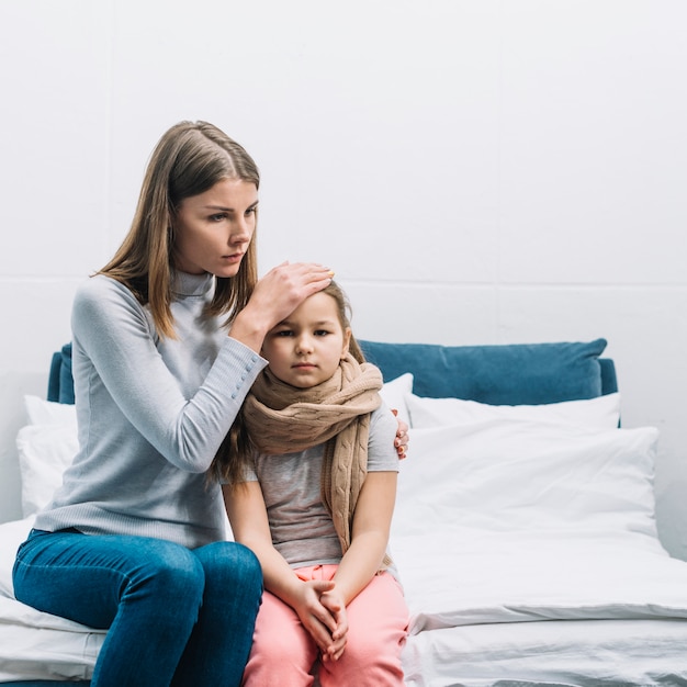 Nahaufnahme einer mutter, die die stirn ihrer tochter berührt, die unter fieber leidet Kostenlose Fotos