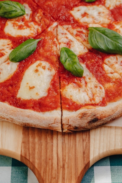 Neapolitanische pizza mit dem schinken, käse, rucola, basilikum, tomaten besprüht mit käse auf einem hölzernen brett auf einer tischdecke in einer zelle Premium Fotos