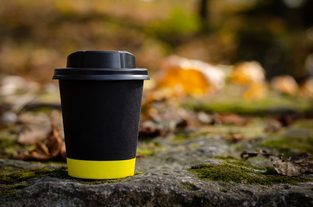 Nehmen sie schwarze kaffeetasse mit dem deckel weg, der draußen auf gefallenem blatthintergrund steht. textfreiraum, verspotten Premium Fotos