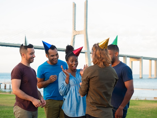 Nette junge leute, die geschenk für überraschtes mädchen geben. lächelnde freunde, die junge frau mit geburtstag beglückwünschen. konzept der geburtstagsfeier Kostenlose Fotos