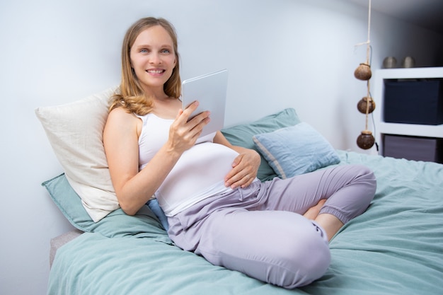 Nette werdende mutter, die tablette im schlafzimmer verwendet Kostenlose Fotos