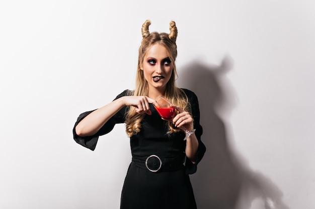 Netter Blonder Vampir Im Kleid Das Auf Weisser Wand Steht Hubsches Schlankes Madchen Das Blut In Halloween Trinkt Kostenlose Foto