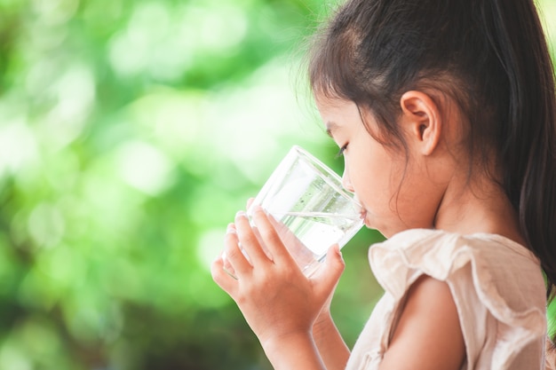 Nettes asiatisches kindermädchen, das süßwasser vom glas trinkt Premium Fotos