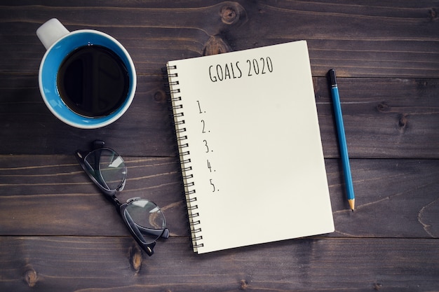 Neujahrsziele, resolution oder aktionsplan 2020. hölzerne tabelle des büros mit leerem notizblock, bleistift, gläsern, telefon und tasse kaffee. Premium Fotos