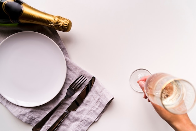 Obenliegende ansicht der menschlichen hand champagnerglas nahe leerer weißer platte auf einfachen hintergrund setzend Kostenlose Fotos