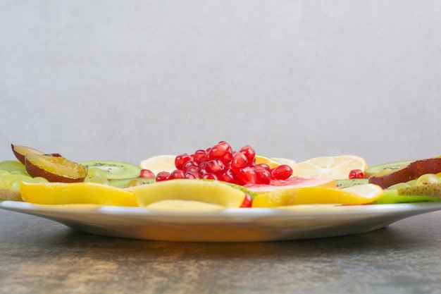 Obstsalat mit granatapfel, grapefruit und kiwi auf weißem teller ...