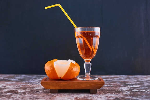 Orange und ein glas saft mit gelber pfeife auf holzplatte