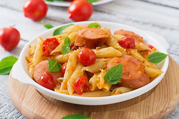 Penne pasta mit tomatensauce mit wurst, tomaten, grünem basilikum in ...