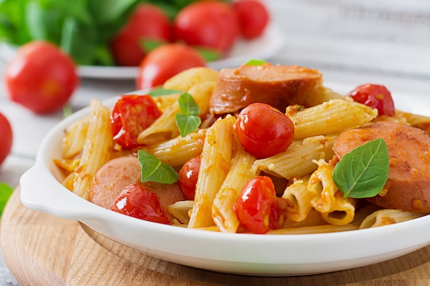 Penne pasta mit tomatensauce mit wurst, tomaten, grünem basilikum in ...