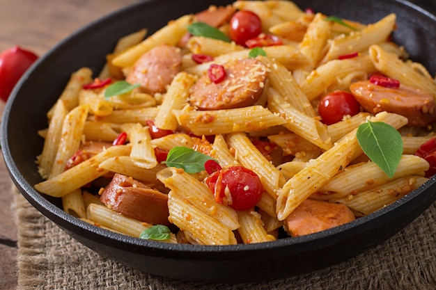 Penne pasta mit tomatensauce mit wurst, tomaten, grünem basilikum in ...