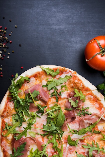 Pizza mit belag von speck und arugula verlässt nahe saftiger tomate und ...