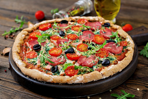 Pizza mit salami, tomaten, oliven und käse auf einem teig mit ...