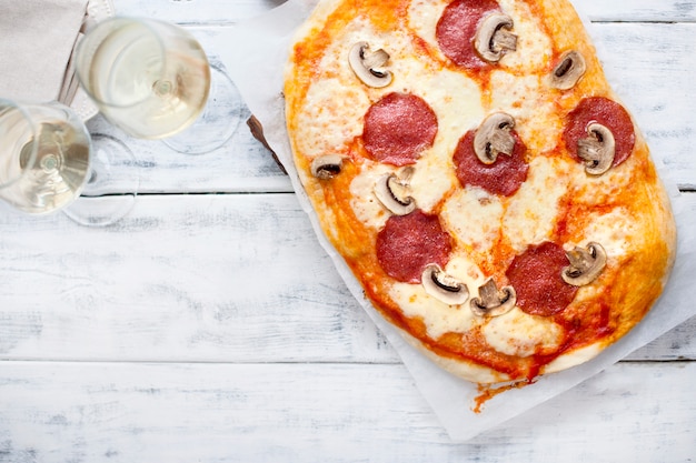 Pizza mit salami und pilzen auf einem weißen hölzernen hintergrund und ...