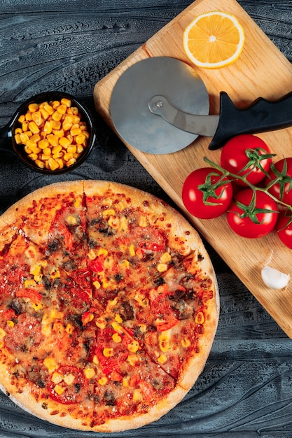 Pizza Mit Tomaten Eine Scheibe Zitrone Und Knoblauch Mais Und Eine Pizzaschneider Hochwinkelansicht Auf Einem Dunklen Holzernen Hintergrund Kostenlose Foto