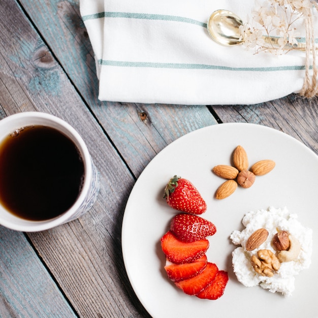 Platte mit hüttenkäse, erdbeeren und nüssen, einem tasse kaffee und tüchern auf holztisch, gesundes lebensmittel, frühstück Premium Fotos