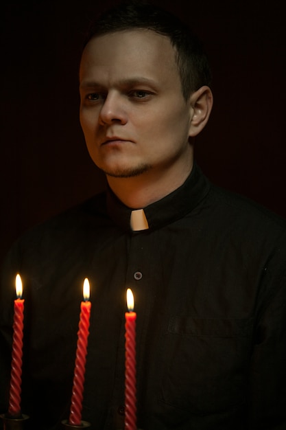 Porträt des hübschen katholischen priesters oder des pastors mit hundehalsband, dunkelroter hintergrund. Premium Fotos