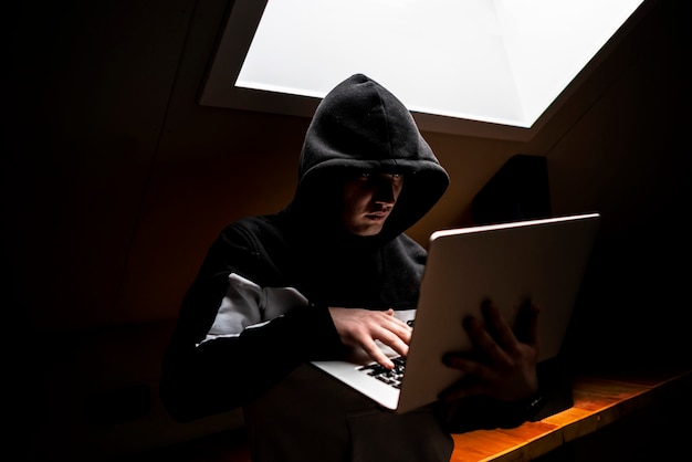 Porträt des jungen aussenseiters in der haube in der dunkelkammer mit laptop Premium Fotos