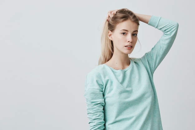 Portrat Einer Gut Aussehenden Jungen Frau Mit Ovalem Gesicht Dunklen Augen Und Hellem Glattem Haar Das Blauen Lassigen Pullover Tragt Nachdenklich Und Selbstbewusst Mit Ihren Haaren Spielend Kostenlose Foto