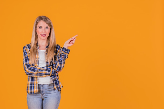 Porträt einer lächelnden jungen frau, die ihren finger gegen einen orange hintergrund zeigt Kostenlose Fotos