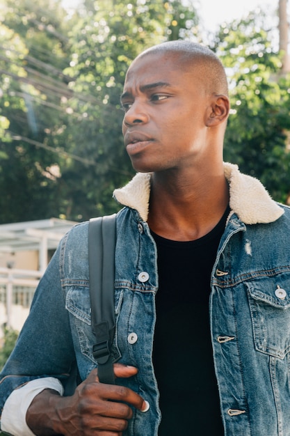 Porträt eines jungen afrikanischen mannes mit rucksack auf seiner schulter, die weg schaut Kostenlose Fotos