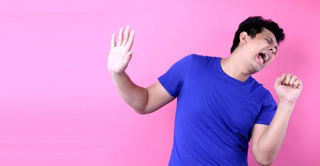 Porträt-hübscher asien-mann, der laut bei der stellung auf rosa hintergrund im studio singt Premium Fotos