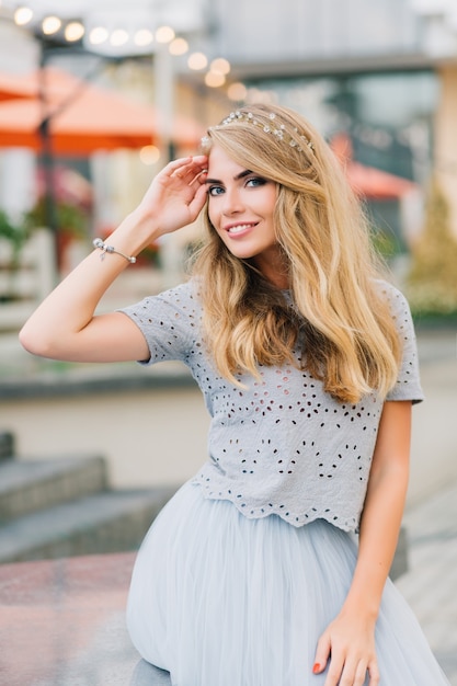 Portrat Schones Madchen Mit Langen Blonden Haaren Im Blauen Tullrock Der Auf Terrassenhintergrund Sitzt Sie Halt Die Hand Auf Dem Kopf Und Lachelt In Die Kamera Kostenlose Foto