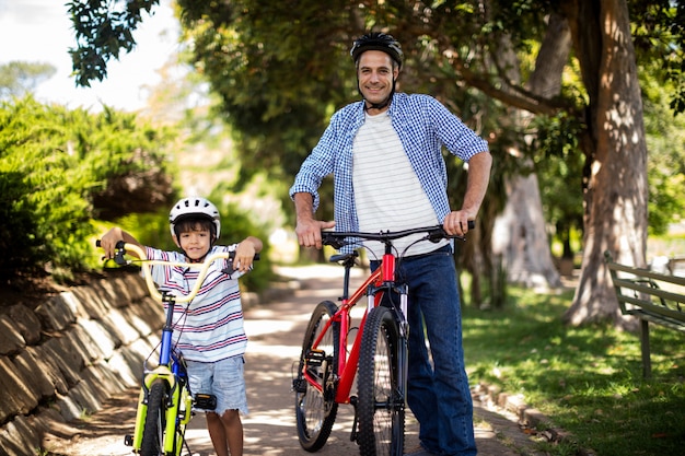 Porträt von vater und sohn, die mit fahrrad im park stehen