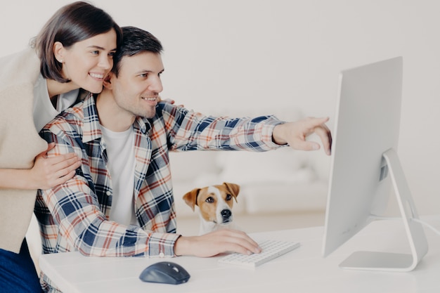 Positive glückliche junge frau und mann arbeiten remote am computer, verbringen gemeinsam ihre freizeit, zeigen auf dem monitor an, buchen online, suchen nach informationen über hotels und planen zukünftige reisen Premium Fotos