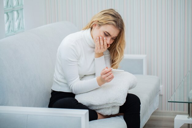 Positiver schwangerschaftstest, junge frau, die nach schwangerschaftstestergebnis zu hause betrachten deprimiert und traurig sich fühlt Premium Fotos
