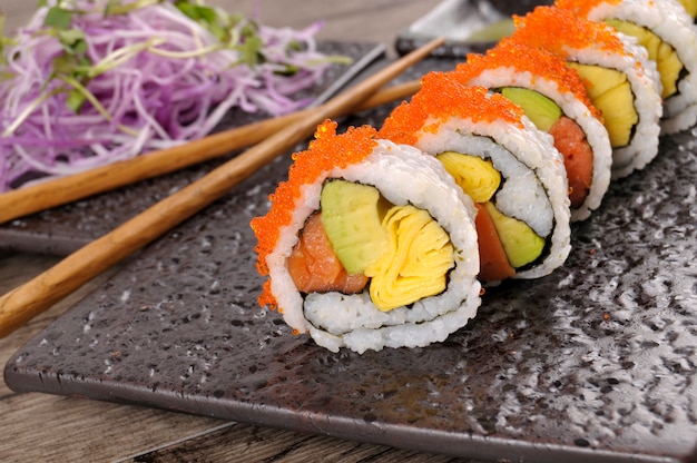 Roll sushi mit stäbchen auf einer schwarzen platte | Kostenlose Foto