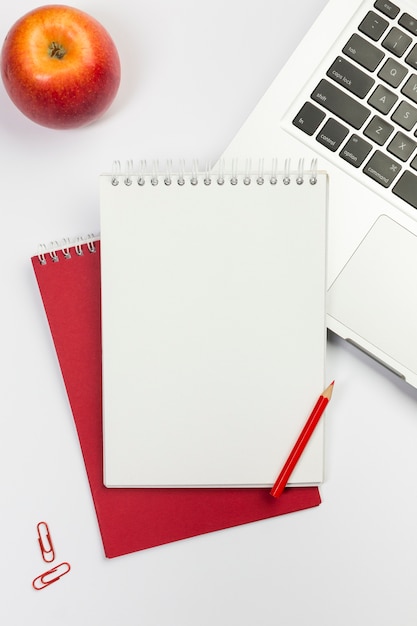 Roter apfel, leerer gewundener notizblock, rote farbbleistift auf laptop über weißem hintergrund Kostenlose Fotos