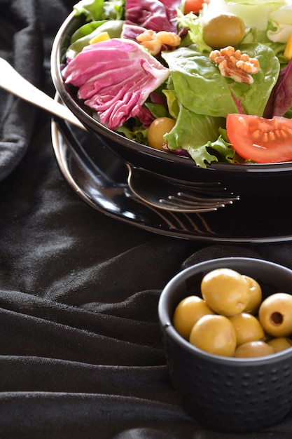 Salatplatte mit salat, tomaten, oliven und öl. auf einem schwarzen tuch ...