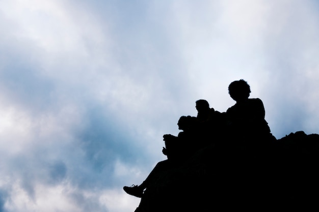 Schattenbild der freunde, die auf felsen gegen blauen himmel sitzen Kostenlose Fotos