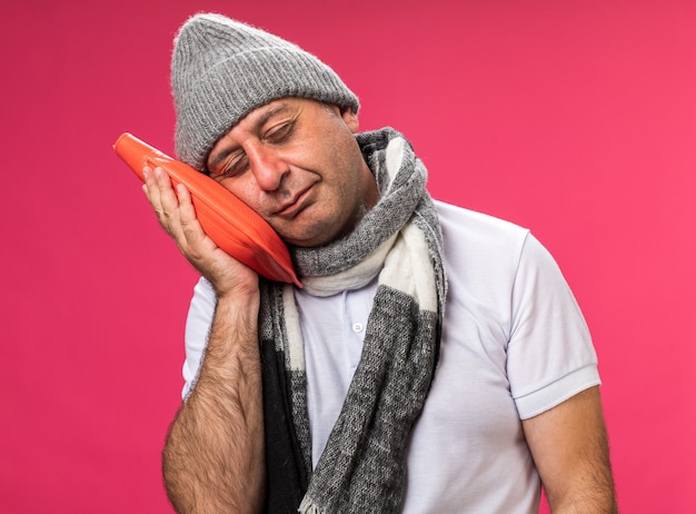 Schlafriger Erwachsener Kranker Kaukasischer Mann Mit Schal Um Den Hals Der Eine Wintermutze Tragt Und Den Kopf Auf Eine Warmflasche Einzeln Auf Rosa Wand Mit Kopienraum Setzt Kostenlose Foto