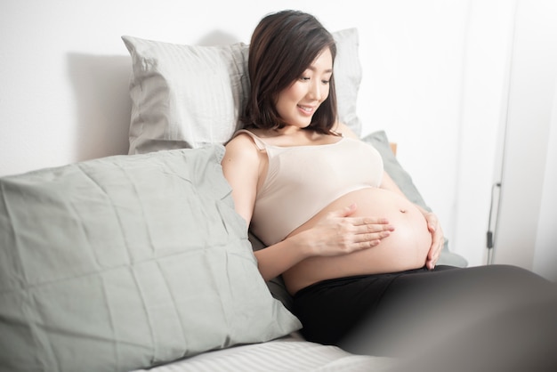 Schöne asiatische schwangere frau, die auf ihrem bett liegt Premium Fotos