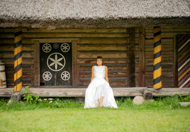 Schöne braut, die nahe dem haus im weißen kleid sitzt