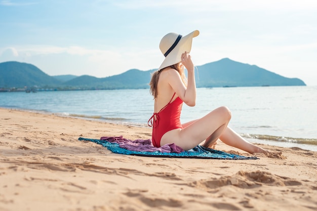 Schöne frau im roten badeanzug sitzt am strand Premium Fotos