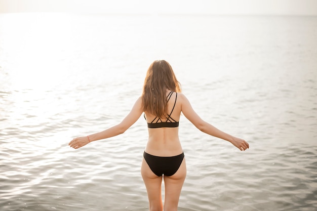 Schöne frau im schwarzen bikini geht auf den strand Premium Fotos