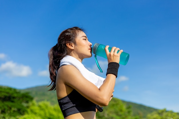 Schöne junge asiatin, die morgens an einer laufbahn, eine pause machend trainiert, um wasser zu trinken Premium Fotos