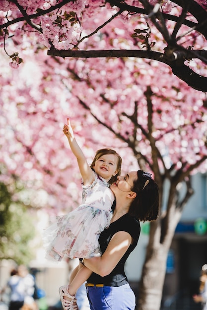 Kostenlos Foto Schone Junge Mutter Halt Die Reizende Kleine Tochter Die Unter Bluhendem Rosa Baum Steht