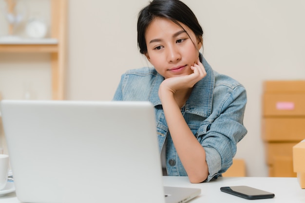 Schöner intelligenter asiatischer jungunternehmergeschäftsfrauinhaber von kmu, das produkt auf lager online überprüft und zum computer speichert, der zu hause arbeitet. Kostenlose Fotos