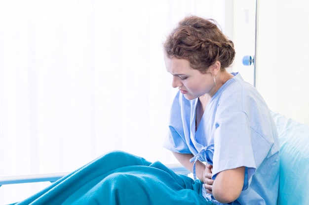 Schöner patient der jungen frau mit zeitraumschmerz auf krankenhausbettraum. Premium Fotos