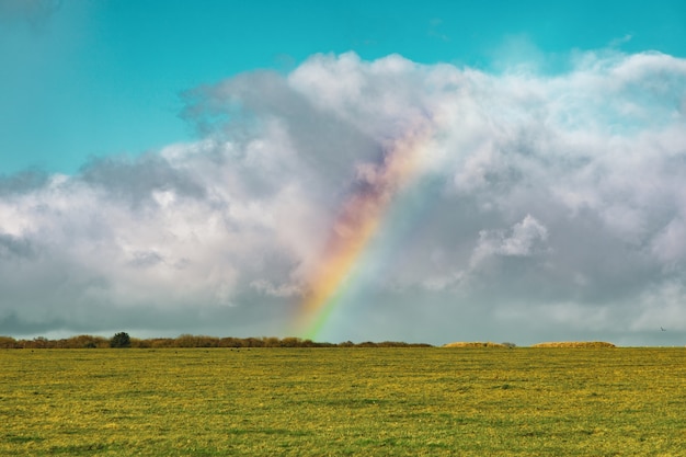 Schoner Schuss Eines Leeren Grasfeldes Mit Einem Regenbogen In Der Ferne Unter Einem Blauen Bewolkten Himmel Kostenlose Foto