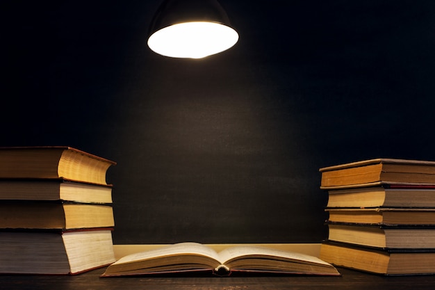 Schreibtisch vor dem hintergrund der kreidetafel, bücher im dunkeln unter dem licht einer lampe. Premium Fotos