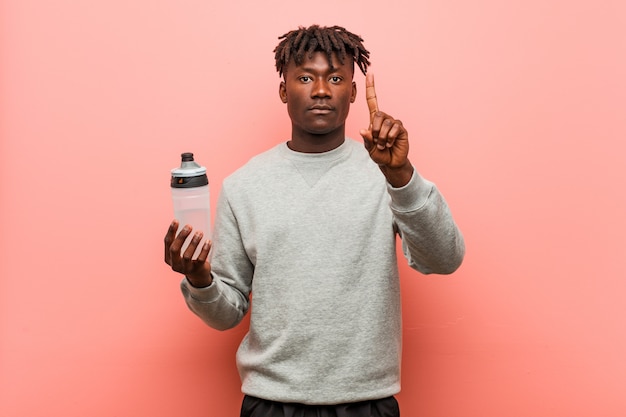 Schwarzer mann der jungen eignung, der eine wasserflasche zeigt nummer eins mit dem finger hält. Premium Fotos