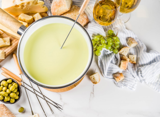 Schweizer feinschmeckerfondue im traditionellen fonduetopf mit gabeln, verschiedenen käsesorten, oliven, brot und trauben Premium Fotos