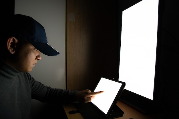 Seitenansicht des mannhackers sitzen am computermonitor, weiße bildschirmtablette, die finger zeigt Premium Fotos