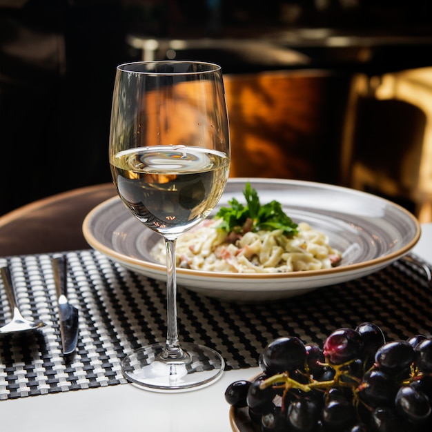 Seitenansicht glas wein mit nudeln und trauben in rundem