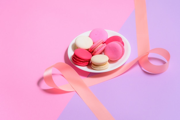 Selbst gemachte bunte makronen oder macaron auf weißer platte auf rosa und purpurrotem hintergrund Premium Fotos