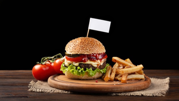 Selbst gemachte hamburgernahaufnahme mit rindfleisch, tomate, kopfsalat, käse und pommes-frites auf schneidebrett. kleine weiße fahne in den burger eingefügt Premium Fotos